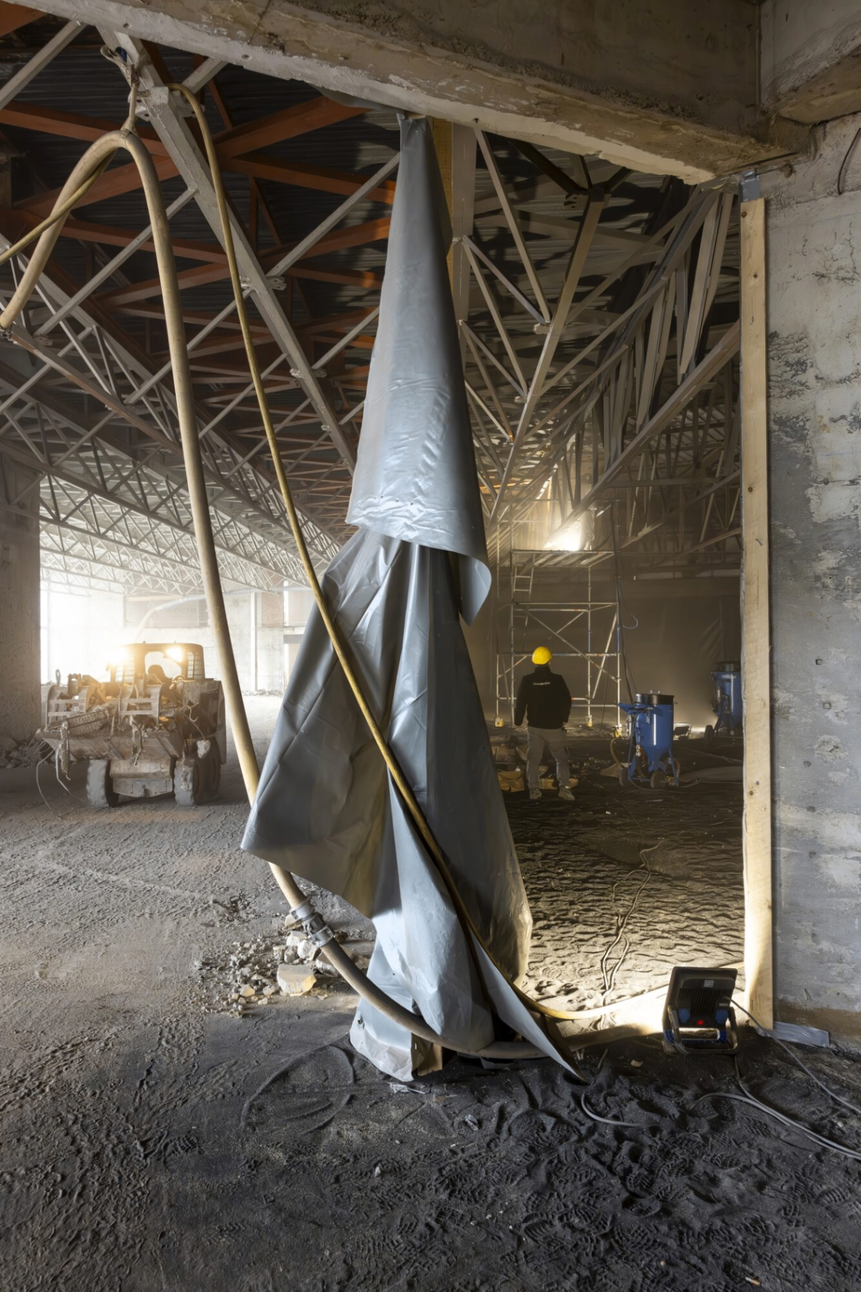 Licht binnenvallend in de Boerentorenwerf met zicht op staalstructuren, machines en een arbeider met gele helm.